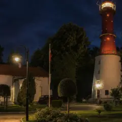 Latarnia morska Jastrzębia Góra nocą, z oświetlonym budynkiem i charakterystyczną czerwoną wieżą.