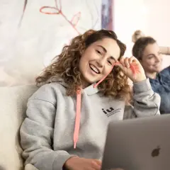 Zwei junge Frauen lernen entspannt. Eine trägt einen Hoodie mit dem Logo der IU Internationale Hochschule, die andere hält ein Tablet.
