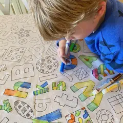 Niño rubio colorea un mantel con letras y dibujos. El **cuadrado para colorear** se llena de vida con sus rotuladores.