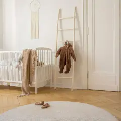 Uroczy, beżowy pokój dla niemowlaka. Białe łóżeczko, drewniana drabinka z brązowym pajacykiem, łapacz snów i okrągły dywanik tworzą przytulną atmosferę.