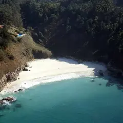Vista aérea de la playa de San Pedro, Galicia, con aguas turquesas, arena blanca y vegetación exuberante en los acantilados.