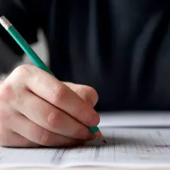 Dłoń pisząca ołówkiem na kartce w kratkę. To może być przygotowanie do wypowiedzi pisemnej matura angielski podstawowy.