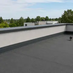 Nowoczesna attyka z szarym obrzeżem i płaskim dachem, widok na zielone drzewa i budynki w oddali.