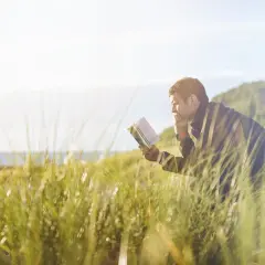 Mężczyzna czyta książkę na ławce wśród traw nad morzem. Czyżby to był **ja inkwizytor kolejność** wydarzeń?