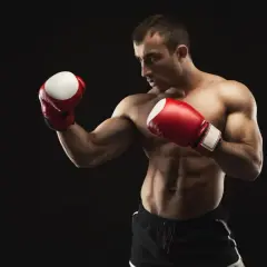 Muscular boxer in red gloves and black shorts in a defensive stance against a black background.