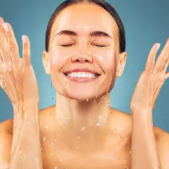 Donna sorridente con acqua sul viso e mani. L'acqua micellare a cosa serve? A detergere e rinfrescare la pelle.