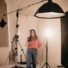 Kobieta z aparatem w studiu fotograficznym, otoczona sprzętem. Pokazuje, jak ustawić lampę błyskową w aparacie, by uzyskać idealne światło.