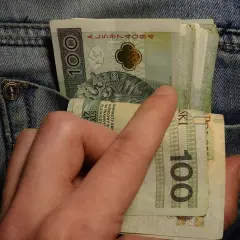 Dłoń wyciąga banknoty 100 zł z kieszeni dżinsów. Może to symbolizować walkę z zatorami płatniczymi lub po prostu gotówkę.