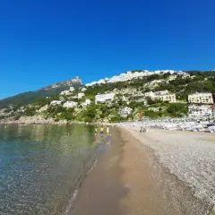 Plage de galets à Vietri sul Mare, Italie, avec des maisons blanches perchées sur la colline verdoyante et la mer bleue étincelante.