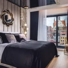 Nowoczesna sypialnia glamour z aksamitnym zagłówkiem, ozdobnym lustrem i widokiem na zabytkowe kamienice.