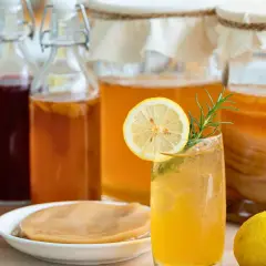 Verre de kombucha rafraîchissant, entouré de bouteilles et de bocaux, rappelant l'origine pays de cette boisson fermentée.