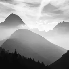 Mgliste pasmo górskie w ujęciu monochromatycznym. W oddali widać ostre szczyty, bliżej łagodne, zalesione wzgórza.