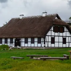 Rzucewo osada łowców fok. Dom z muru pruskiego i strzechą, otoczony zielenią, z ławkami i stołem w trawie.