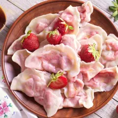 Pyszne pierogi z truskawkami, ozdobione świeżymi owocami, wyglądają apetycznie na glinianym talerzu.