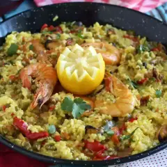 Arroz con pollo y marisco en paellera, adornado con limón y perejil. Un festín de sabores.