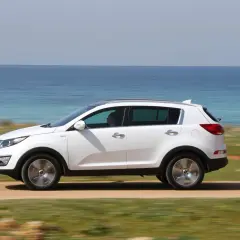 Biały Kia Sportage 2012 jedzie po drodze nad morzem.