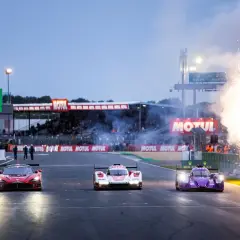 Tres coches de carreras compiten en Le Mans, con fuegos artificiales iluminando la pista. El horario de Le Mans se acerca.