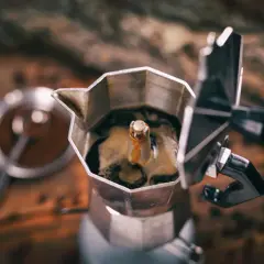 Caffettiera moka in primo piano, con il caffè che sale. Un rituale mattutino che, si dice, il caffè aiuta a digerire.