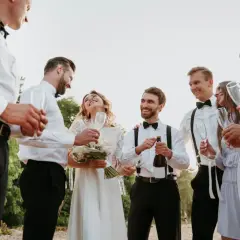 Pan młody otwiera szampana, a jego świadek i druhna wznoszą toast. Wszyscy uśmiechnięci, świętują ten wyjątkowy dzień.
