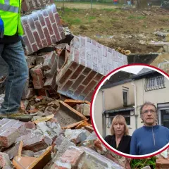 Pareja preocupada frente a los escombros de su hogar tras un cru catastro. Un trabajador con chaleco fluorescente camina entre los restos.