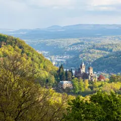 Majestätische Burg Drachenfels thront über einem grünen Tal mit einem Fluss und weiteren Burgen.