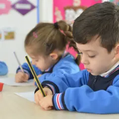 Niños concentrados en sus cuadernos, un momento de aprendizaje y adaptación en el aula.