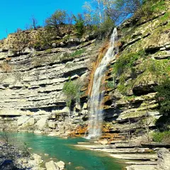 Cascate di Moraduccio: una cascata scende da una parete rocciosa stratificata, formando un arcobaleno nell'acqua turchese sottostante.
