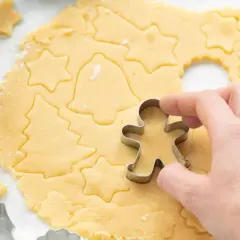 Mit diesem Kekse Rezept entstehen Sterne, Tannenbäume und Lebkuchenmännchen. Ein Holz-Nudelholz liegt daneben.