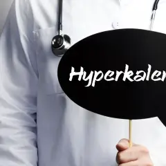 Lekarz w białym fartuchu ze stetoskopem trzyma czarną chmurkę z napisem "Hyperkalemia".
