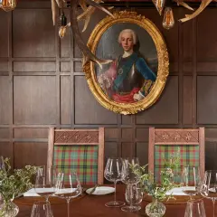 Un ritratto regale domina la sala da pranzo, con sedie a quadri e un tavolo apparecchiato, un'ambientazione che evoca i migliori ristoranti di Londra.