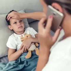 Chory chłopiec leży pod kocem, mama sprawdza mu temperaturę i dzwoni po pomoc. L4 na dziecko.