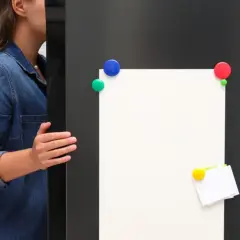 Kobieta w dżinsowej koszuli otwiera drzwi lodówki z pustą kartką i kolorowymi magnesami.