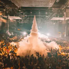 Folla in delirio in una **fabrik discoteca** con un getto di fumo che sale verso il soffitto.