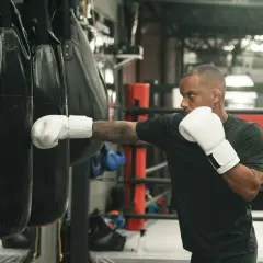 Man in white boxing gloves throws a punch at a heavy bag, demonstrating how to practice boxing without a bag.