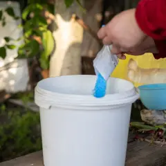 Une main verse une poudre bleue dans un seau blanc. C'est la préparation de la bouillie bordelaise pour protéger les plantes.