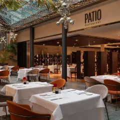 Atmosfera elegante al Patio Restaurant, un'ottima opzione per chi cerca dove mangiare a Bolzano. Tavoli apparecchiati sotto luci soffuse e piante rigogliose.