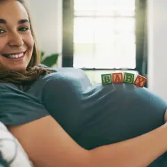 Uśmiechnięta surogatka z klockami "BABY" na brzuchu.
