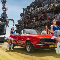 Trzy cheerleaderki z pomponami pozują przy czerwonym kabrioletcie na tle sterty złomu. To może być ciekawy widok dla kogoś szukającego auto szrot bydgoszcz.