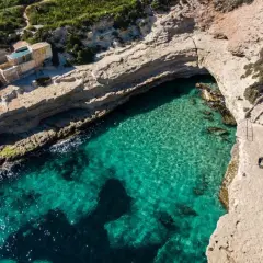 Malta plaże: turkusowa woda, skaliste wybrzeże i mały domek nad zatoczką. Dwie osoby spacerują ścieżką.