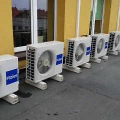Rząd białych jednostek klimatyzacyjnych Haier na dachu, obok żółtej ściany budynku.