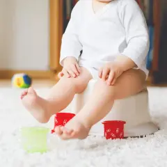 Liten bebis på pottan, redo att sluta med napp. Färgglada leksaker och en mjuk matta skapar en trygg miljö för potträning.