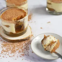 Tiramisu en verrine saupoudré de cacao, avec une cuillère garnie.