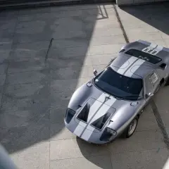 Srebrny Ford GT40 z białymi pasami, gotowy do wyścigu. Ikona motoryzacji na betonowym placu.