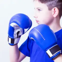 Young boxer in a wide boxing stance, wearing blue gloves and shirt, ready to fight.
