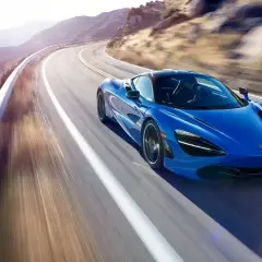 Niebieski McLaren 720S pędzi po krętej górskiej drodze, tworząc rozmyte smugi światła i cienia.