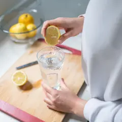 Eine Hand presst eine Zitronenhälfte über ein Glas Wasser. So beginnt der Tag mit erfrischendem Zitronenwasser.