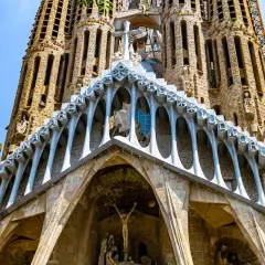 Intricate Gaudi art adorns the Sagrada Familia, with stone carvings and arched facades reaching towards a bright blue sky.