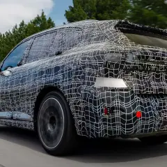La nuova BMW X5 2026, con la sua mimetica di test, sfreccia su una strada panoramica, anticipando il futuro del design.