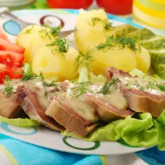 Pokrojone ozory wieprzowe w sosie, podane z ziemniakami, pomidorami i ogórkiem kiszonym.
