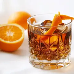 En drink med is och apelsinskal, bredvid apelsiner. Perfekt för ett sockerlag recept.